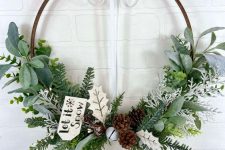 a natural Christmas wreath decorated with greenery, evergreen, leaves, bells, pinecone and a tag is a lovely decor idea