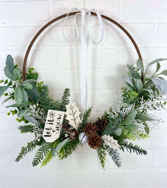 a natural Christmas wreath decorated with greenery, evergreen, leaves, bells, pinecone and a tag is a lovely decor idea
