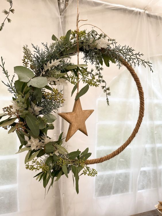 a natural holiday wreath wrapped with rope, with a wooden star, greenery, evergreens and white blooms