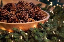 a pinecone Christmas centerpiece of a wooden bowl, pinecones, an evergreen wreath with lights is cozy and natural