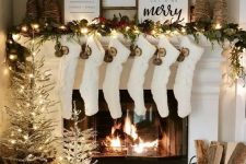 a pretty and shiny Christmas mantel with an evergreen and light garland, yarn Christmas trees, dried fruit slices, white stockings