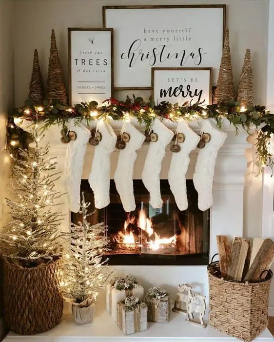 a pretty and shiny Christmas mantel with an evergreen and light garland, yarn Christmas trees, dried fruit slices, white stockings