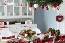 a red and white Christmas chandelier, a red table runner and berries for decor create a holiday atmosphere