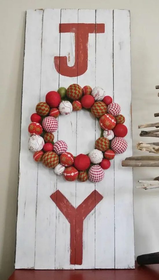 a red and white wooden plaque Christmas sign with red letters and a round O letter composed of Christmas ornaments in red and white