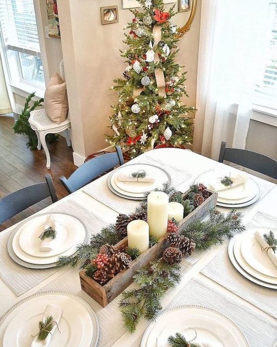 a simple neutral Christmas tablescape with silver chargers, white plates, evergreens and pinecones, berries and candles