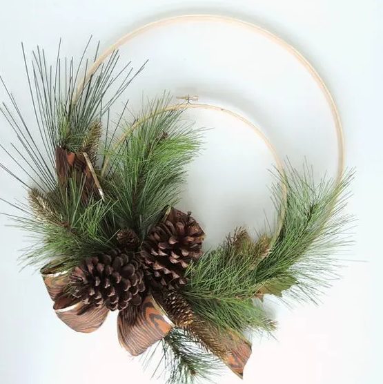 a simple rustic Christmas wreath of two embroidery hoops, evergreens, pinecones and a printed ribbon bow is cool