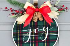a super cool and easy to make Christmas wreath with green plaid, a red and neutral ribbon bow on top, evergreens and berries