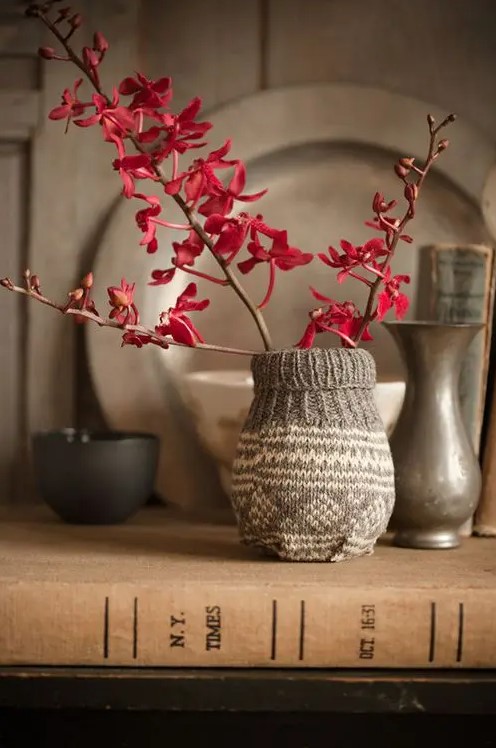 a vase wrapped with a knit piece and branches with burgundy blooms on it looks laconic and cozy