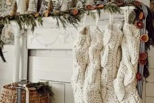 a whimsy Christmas mantel with an evergreen and dried fruit slice garland, mini Christmas trees and oversized white stockings