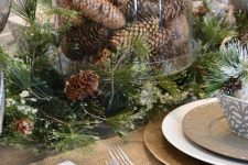 a woodland Christmas tablescape with a centerpiece of evergreens and pinecones in a clear in cloche is a cool idea