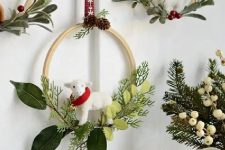 an arrangement of small embroidery hoops with evergreens, red berries and leaves plus sheep hanging on red ribbons