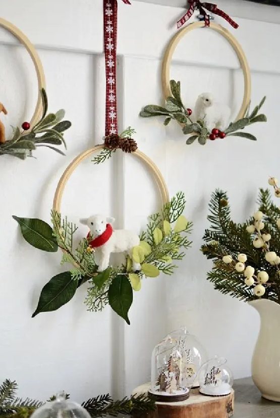 an arrangement of small embroidery hoops with evergreens, red berries and leaves plus sheep hanging on red ribbons