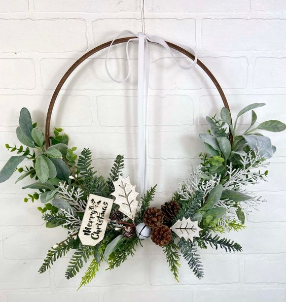an embroidery hoop holiday wreath with evergreens, leaves, pinecones and a tag is a cool idea for the holidays
