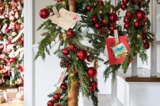 beautiful Christmas banister decor with an evergreen garland, red ornaments, pinecones and Christmas postcards