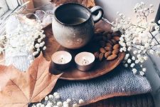 cozy and simple fall Nordic decor with a stack of blankets, baby’s breath and leaves, candles, nuts and coffee