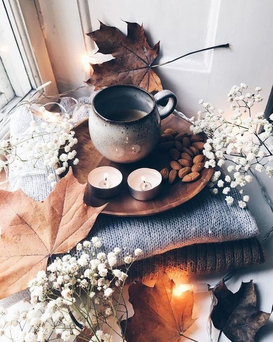 cozy and simple fall Nordic decor with a stack of blankets, baby's breath and leaves, candles, nuts and coffee