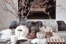 elegant Scandinavian fall home decor with dried branches in a vase, a candle lantern and some pumpkins on the faux fur
