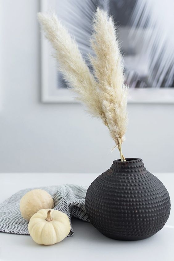 laconic Scandianvian fall decor with a black vase and pampas grass, white pumpkins and a towel is cool