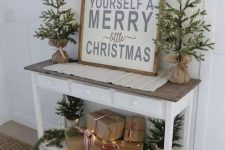little trees in burlap and some in buckets on the console plus s a rustic Christmas sign for a farmhouse feel