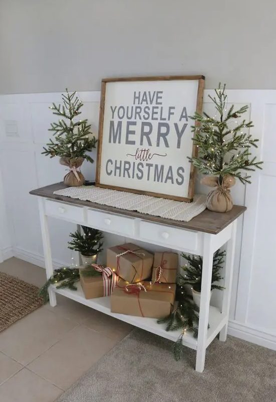 little trees in burlap and some in buckets on the console plus s a rustic Christmas sign for a farmhouse feel