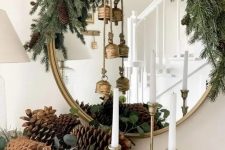 pretty Christmas decor with evergreens, pinecones, vintage brass bells, tall and thin candles is a lovely idea