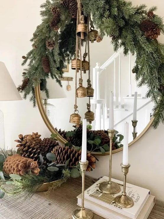 pretty Christmas decor with evergreens, pinecones, vintage brass bells, tall and thin candles is a lovely idea