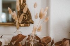 simple Scandinavian fall decor with leaves, grasses in clear vases and white pumpkins is a cool and chic idea