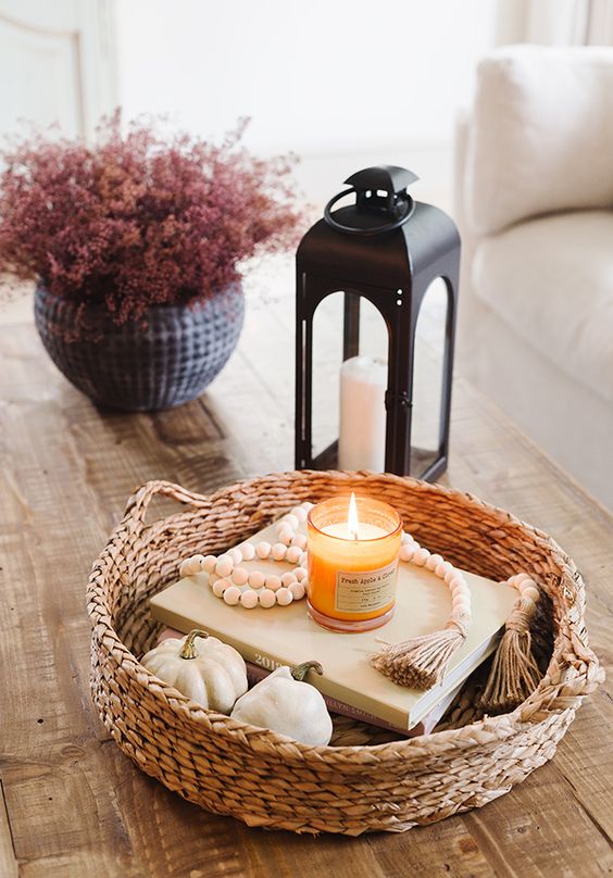 stylish Scandinavian fall decor with a basket, pumpkins, books, wooden beads, a candle, a candle lantern and some pink blooms in a planter