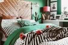 04 a catchy eclectic bedroom with emerald walls, a bed with a wooden headboard, colorful and printed bedding, a beaded chandelier, a pink lamp and some cacti