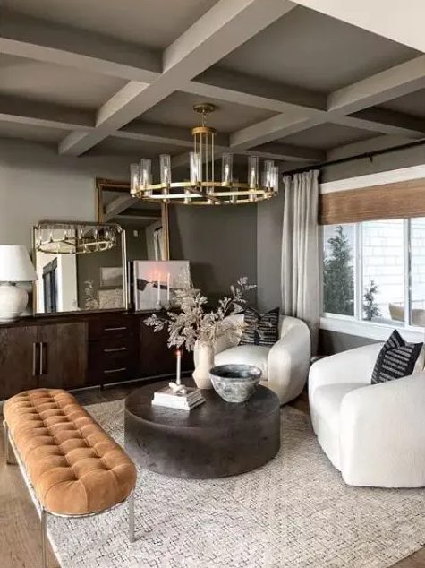 a sophisticated living room in earthy tones, with grey walls and a ceiling, a dark-stained credenza, white chairs, a round coffee table and a rust-colored upholstered bench