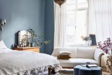 10 a lovely eclectic bedroom with navy walls, a bed with neutral bedding, a dark green bench, a white loveseat and a Moroccan lamp