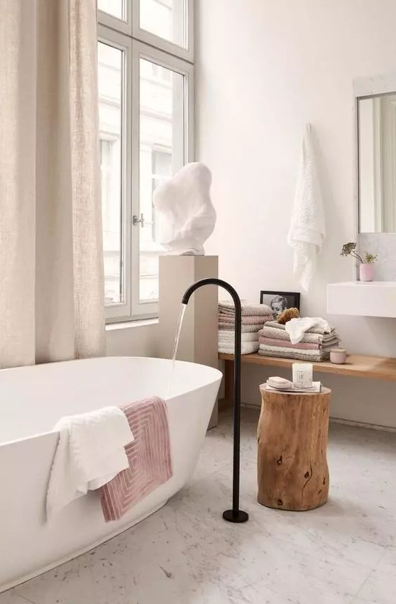 a lovely spa bathroom with an oval tub and a black faucet, a floating shelf, a wall-mounted sink and a sculpture on a stand