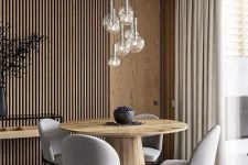 13 a contemporary dining space with a wood slat accent wall, a round wooden table, grey chairs, a cluster of pendant lamps