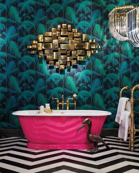 a maximalist bathroom with a tropical leaf wall, a black and white geometric floor, a hot pink tub and gold touches