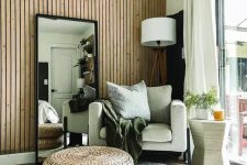 19 a lovely boho space with a wood slat accent wall, a neutral chair, a floor lamp, a mirror, layered rugs and jute poufs