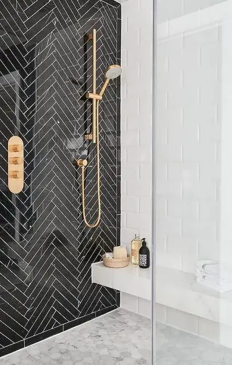 black herringbone tiles with white grout for accentuating the shower space and brass touches for a chic look