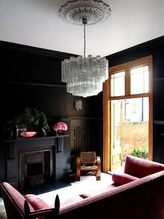 a black living room with a pink sofa, a vintage fireplac,e a crystal chandelier and some pink decor