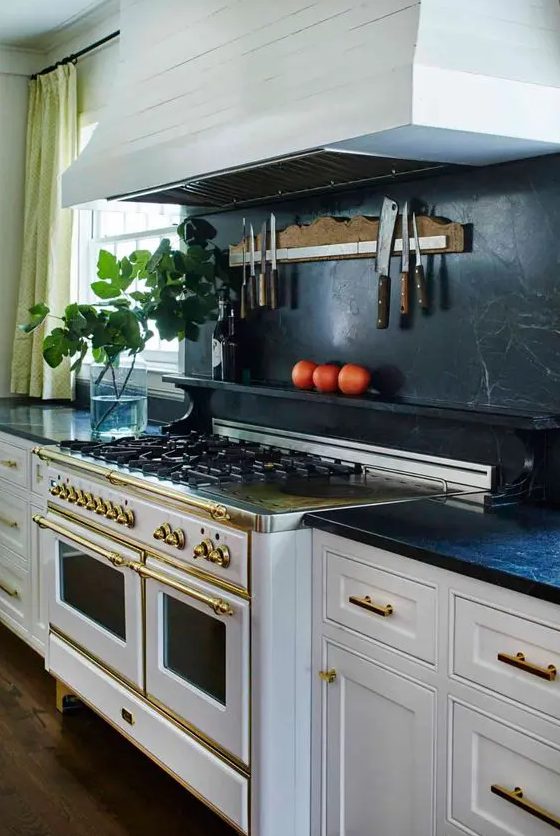 a vintage white kitchen with shaker cabinets, black soapstone countertops and a backsplash, gold touches and fixtures
