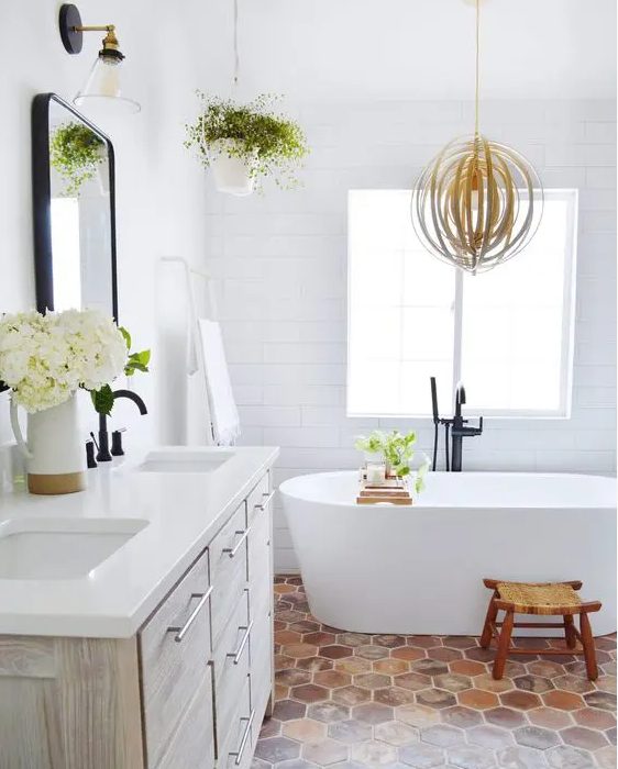 a modern farmhouse bathroom with white tile walls and a terracotta hex tile floor, a whitewashed vanity, an oval tub and greenery