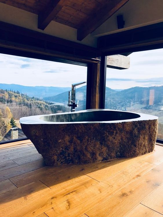 a rustic bathroom with a fantastic view, wooden floors and a dark stone bathtub carved of a single piece of stone