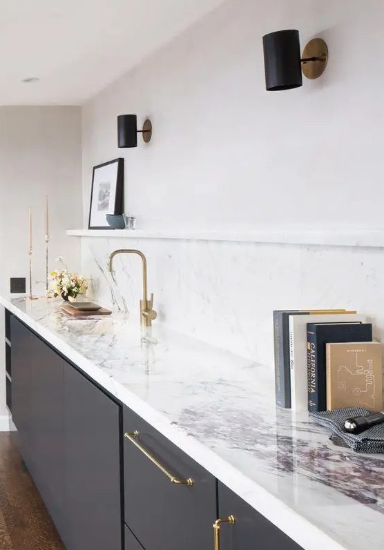 a charcoal grey kitchen with a white quartz backsplash and countertops plus gold fixtures and black spotlights