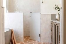 30 a neutral bathroom clad with white Zellige tiles, with a shower space and an oval tub, a terracotta tile floor, a stained vanity