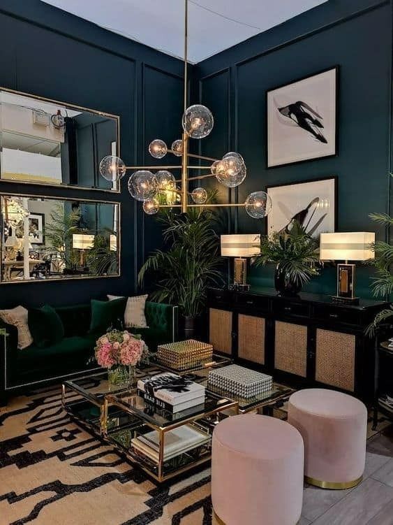 a chic moody living room with navy walls, a green sofa, a black credenza, pink poufs and a glass coffee table
