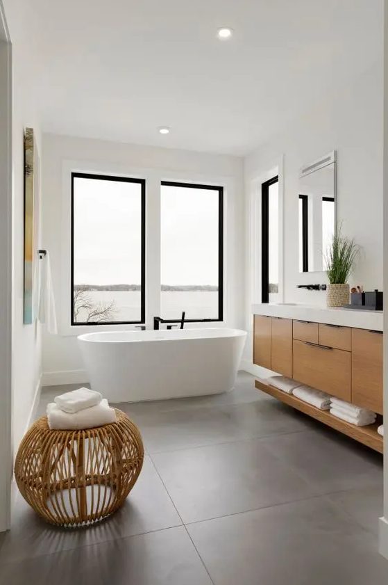 a contemporary bathroom with windows, large scale tiles, a timber vanity, a rattan pouf and some artwork