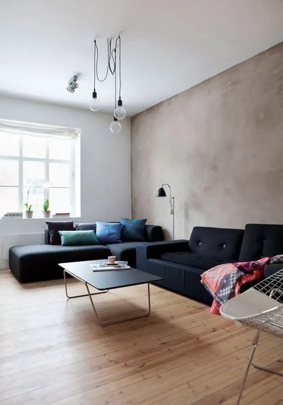a modern living room with a greige limewashed wall, black sofas and colorful pillows, pendant bulbs and a black sconce