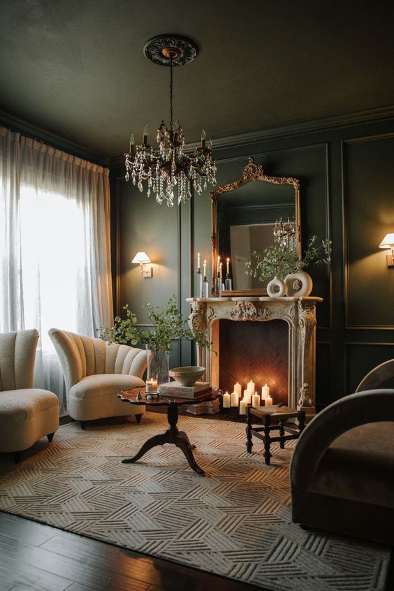 a moody dark green living room with an antique fireplace with candles, a chic crystal chandelier and refined furniture