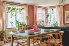 42 a pink open layout with an emerald sofa, a table and woven chairs, potted greenery and bright artwork