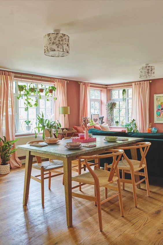 a pink open layout with an emerald sofa, a table and woven chairs, potted greenery and bright artwork