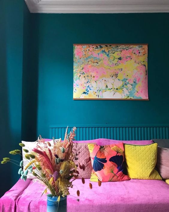 a bright teal living room with a hot pink sofa and colorful pillows, bright dried grasses and blooms are really about dopamine