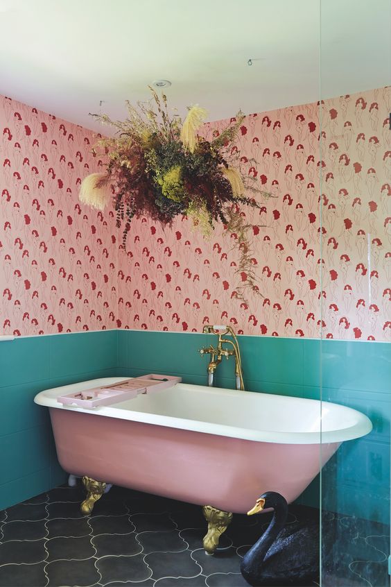 a bright 'dopamine' bathroom with bold printed wallpaper, green tile, a pink bathtub a dried grass chandelier
